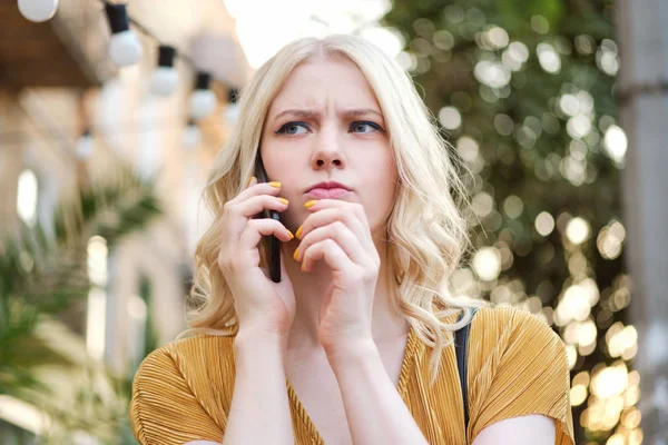 Портрет расстроенной блондинки, задумчиво глядящей в сторону и разговаривающей по мобильному телефону — стоковое фото