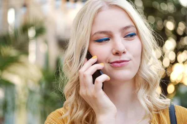 Портрет красивой кокетливой блондинки, коварно глядящей в сторону и говорящей по мобильному телефону. — стоковое фото