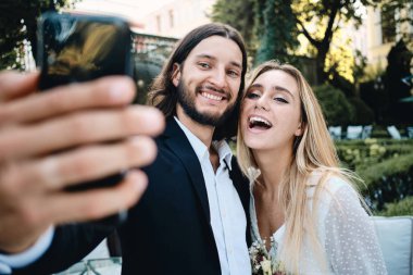 Genç çekici neşeli damat ve gelin mutlu restoran bahçesinde birlikte selfie alarak