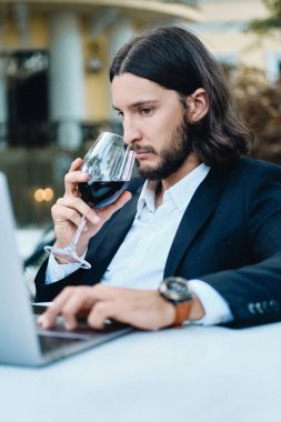 Genç çekici esmer sakallı işadamı düşünceli restoran açık dizüstü bilgisayar üzerinde çalışan şarap içme