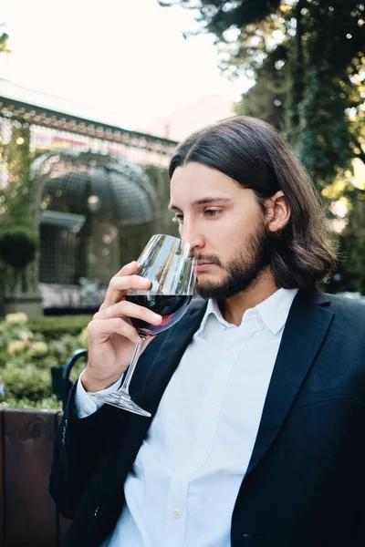Young handsome pensive brunette bearded man thoughtfully drinking red wine in restaurant outdoor — Stock Photo, Image