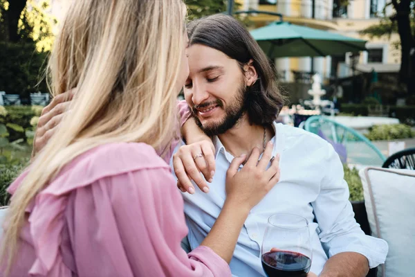 Молода приваблива брюнетка бородатий чоловік у сорочці з келихом вина мрійливо обіймає дівчину на романтичному побаченні в ресторані на відкритому повітрі — стокове фото