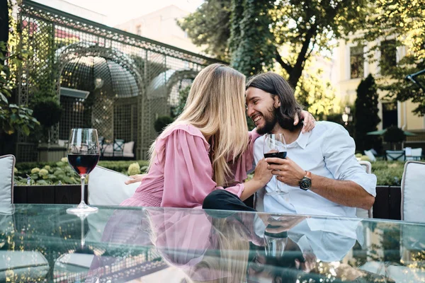 Hermosa pareja romántica bebiendo alegremente vino tinto en la fecha en el restaurante al aire libre — Foto de Stock