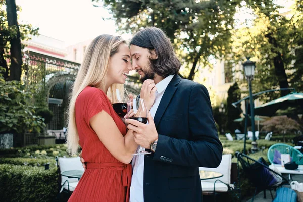Όμορφο ρομαντικό ζευγάρι με τα ποτήρια του κόκκινου κρασιού αγκαλιασμένοι καλά στην ημερομηνία στο εστιατόριο υπαίθρια — Φωτογραφία Αρχείου