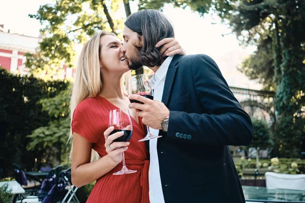 Νεαρό όμορφο ζευγάρι με γυαλιά κόκκινου κρασιού φιλιά το ένα στο άλλο Γιορτάζοντας την αφοσίωση στο εστιατόριο υπαίθρια — Φωτογραφία Αρχείου