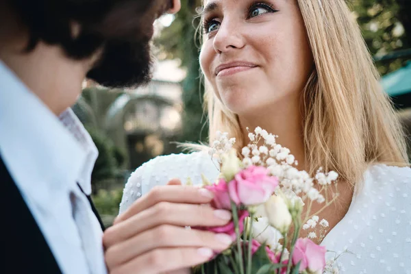 Close-up mooie blonde bruid met boeket bloemen dromerige kijken naar de bruidegom buiten — Stockfoto