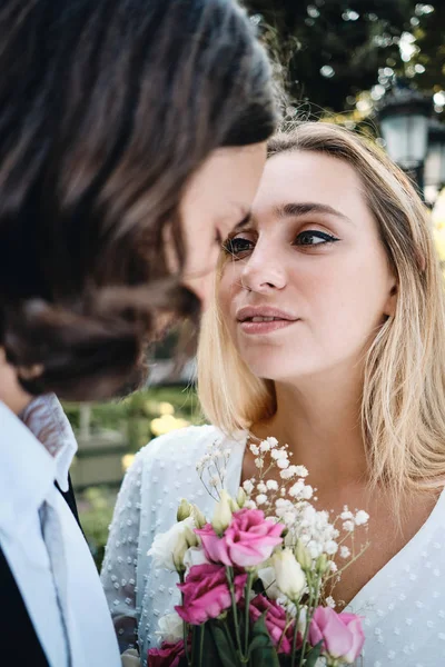 Close-up mooie blonde bruid met boeket bloemen sensueel op zoek naar knappe bruidegom buiten — Stockfoto