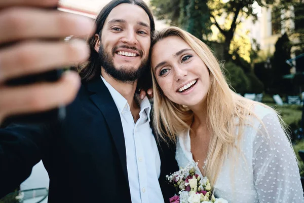 Unga attraktiva leende brudgum och brud glatt tar Selfie tillsammans utomhus — Stockfoto