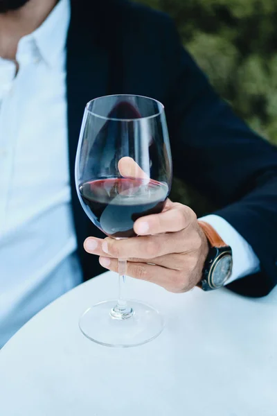 Cerca de mano masculina sosteniendo copa de vino tinto en el restaurante al aire libre — Foto de Stock