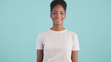 Güzel, gülümseyen Afro-Amerikan kadının portresi mavi arka planda kamerada iyi bir jest gösteriyor.