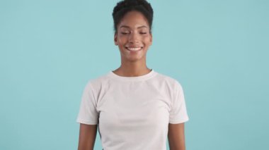 Neşeli Afro-Amerikan kız portresi mavi arka planda kameraya seviniyor.