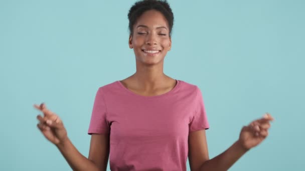 漂亮的微笑着的非洲裔美国女孩高兴地交叉着手指 满怀希望地在蓝色的背景下对着镜头许愿 — 图库视频影像