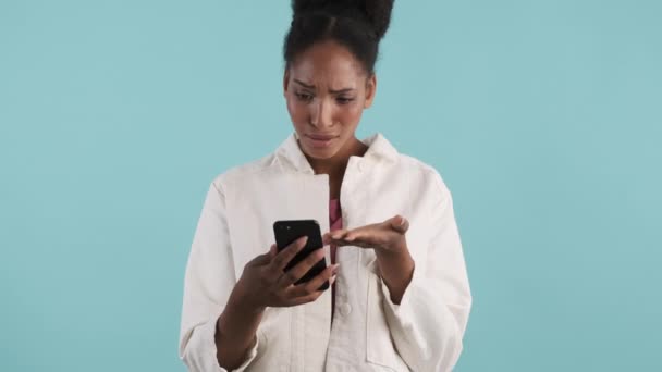 Upset African American Girl Disappointedly Looking Cellphone Blue Background — Stock Video