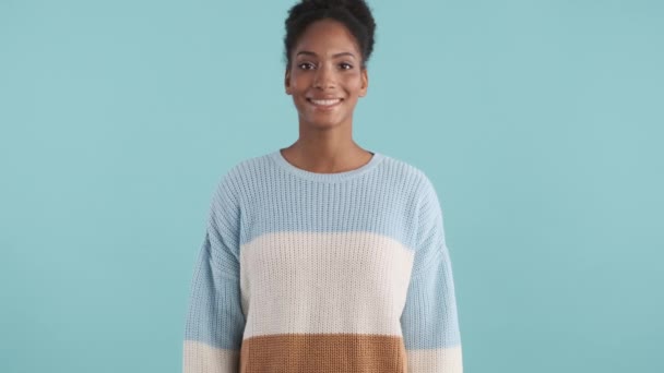 魅力的な陽気なアフリカ系アメリカ人の女の子で居心地の良いセーター喜んで見ますカメラで青の背景 — ストック動画