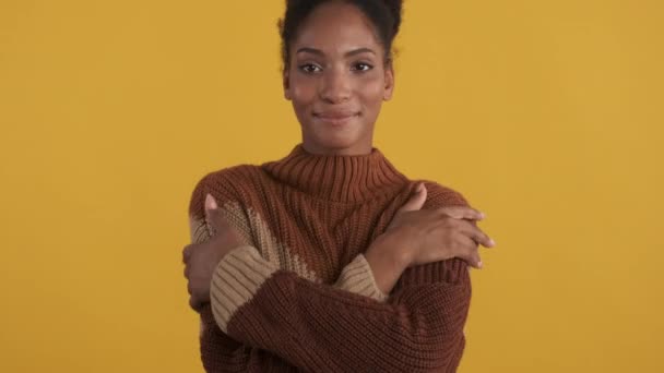 魅力的な柔らかいアフリカ系アメリカ人の女の子の肖像画でニットセーター喜んで楽しいです暖かい見てでカメラの上に黄色の背景 — ストック動画