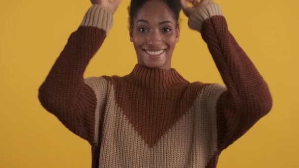 明るいですアフリカ系アメリカ人の女の子の肖像でニットセーター喜んで周りにカメラ上の黄色の背景 — ストック動画