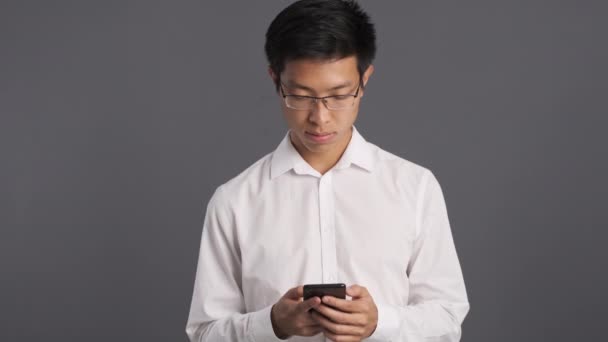 Gözlüklü Yakışıklı Asyalı Genç Adam Gri Arka Planda Cep Telefonu — Stok video