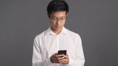 Gözlüklü ciddi bir Asyalı cep telefonu kullanıyor.