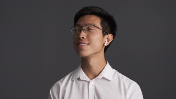 Gözlüklü Yakışıklı Asyalı Genç Adam Gri Arka Plan Üzerinde Kablosuz — Stok video