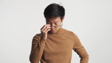 Genç üzgün Asyalı adam gözlüğünü çıkartıyor ve kamerada yalnız poz veriyor.