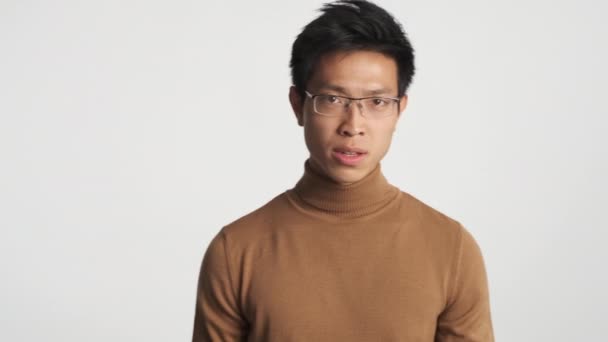 年轻的怒气冲冲的亚洲人 戴着眼镜 在白色背景下对着摄像机怒气冲冲 狂怒的表情 — 图库视频影像