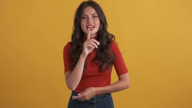 Kırmızı bluzlu güzel esmer kız renkli arka planda sessizlik jesti gösteriyor. Gizli ifadeyi koru