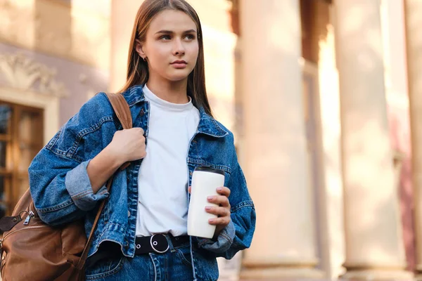 Ung attraktiv elegant casual student flicka i denim jacka med ryggsäck eftertänksamt tittar bort utomhus — Stockfoto
