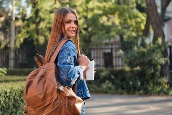 Bella studentessa casual in giacca di jeans con zaino gioiosamente cercando nella fotocamera in outdoo universitario — Foto Stock