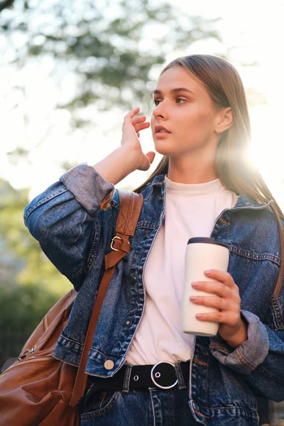 Sırt çantası ve bardağı olan kot ceketli, düşünceli, sıradan bir öğrenci.