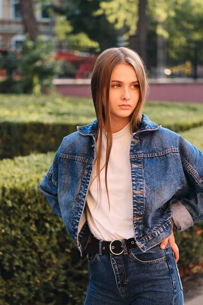 Linda menina de cabelos castanhos casuais graves em jaqueta jeans pensativo olhando para longe ao ar livre — Fotografia de Stock
