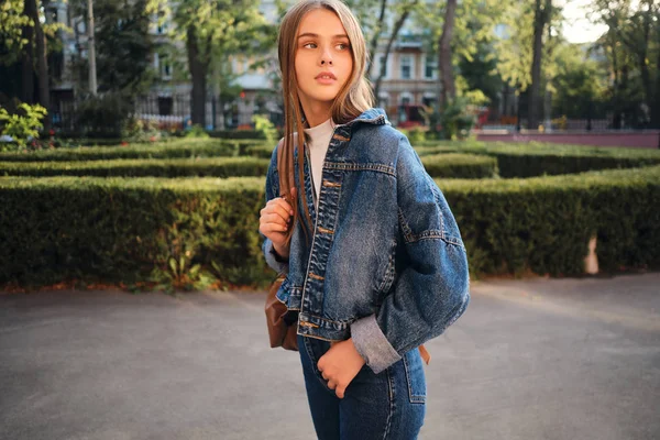 Красивая стильная случайная девушка в джинсовой куртке задумчиво смотрит на улицу — стоковое фото