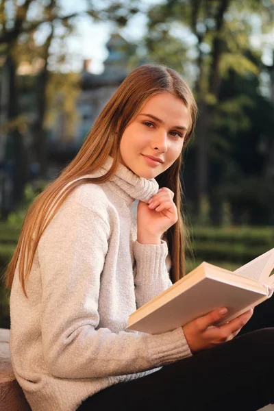 Muda cukup tersenyum gadis mahasiswa dalam sweater nyaman sensual melihat ke kamera belajar dengan buku outdoor — Stok Foto