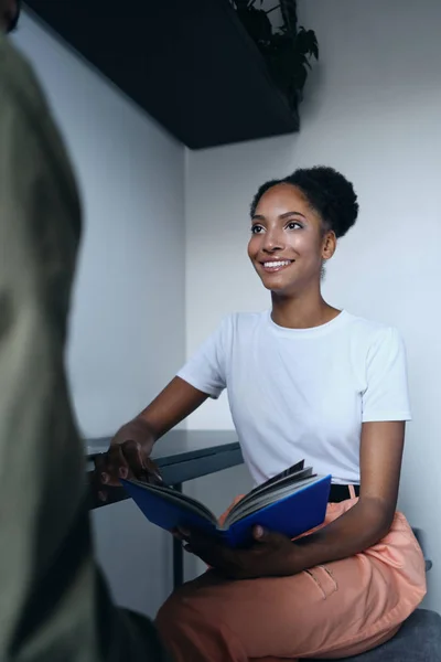 Giovane bella sorridente donna afro-americana casuale che parla con gioia con il collega in un moderno spazio di co-working — Foto Stock