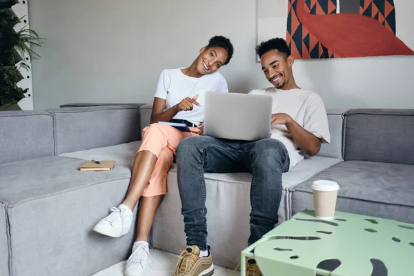 Fiatal vonzó vidám Fiatal vonzó alkalmi afro-amerikai pár boldogan dolgozik laptop együtt a modern otthon afro-amerikai pár boldogan — Stock Fotó