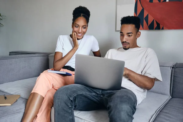 Fiatal izgatott alkalmi afro-amerikai pár boldogan dolgozik laptop együtt kanapén modern otthon — Stock Fotó