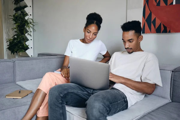 Fiatal vonzó alkalmi afro-amerikai pár gondolkodva dolgozik laptop együtt kanapén modern otthon — Stock Fotó