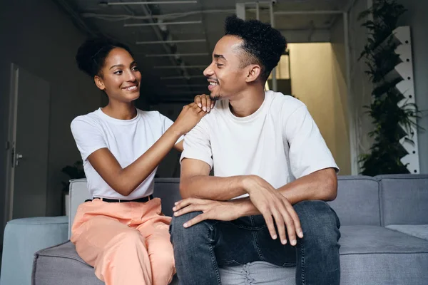 Fiatal vonzó vidám alkalmi afro-amerikai pár boldogan nézik egymást a kanapén a modern otthon — Stock Fotó