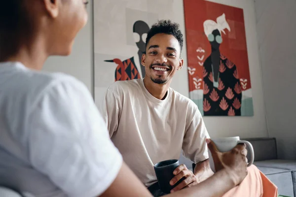 Fiatal vonzó mosolygós alkalmi afro-amerikai férfi örömmel néz kamerába kávészünet közben a modern co-working térben — Stock Fotó