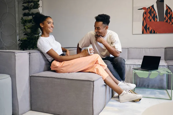 Mladý atraktivní radostný afroamerický pár šťastně mluví během přestávky na kávu v moderním co-working prostoru — Stock fotografie