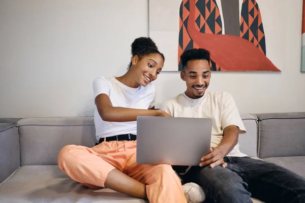 Mladý radostný afroamerický pár šťastně pomocí notebooku spolu na pohovce v moderním kopracovním prostoru — Stock fotografie