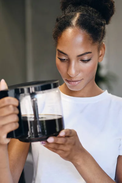 Egy csinos afro-amerikai lány portréja, aki figyelmesen tartja a kávéfőzőt az irodában. — Stock Fotó