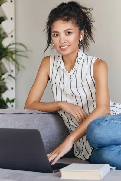 Bella ragazza asiatica casuale felicemente alla ricerca in macchina fotografica di lavoro sul computer portatile a casa moderna — Foto Stock