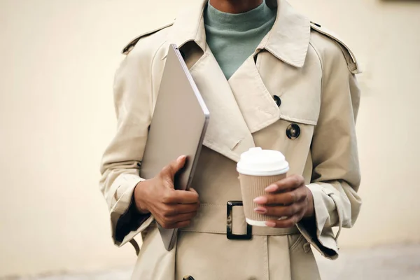 Close up casual woman in stylish trench coat with laptop and coffee to go outdoor — 图库照片