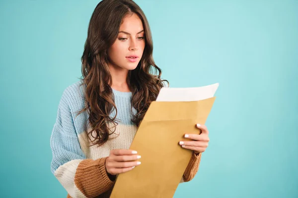 Aantrekkelijk meisje in gezellige trui bedachtzaam openen reactie envelop over blauwe achtergrond — Stockfoto