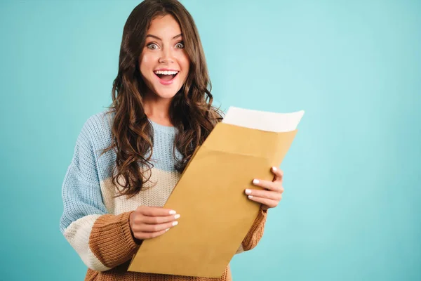 Attraente ragazza eccitata in accogliente maglione apertura risposta busta gioiosamente cercando nella fotocamera su sfondo blu — Foto Stock