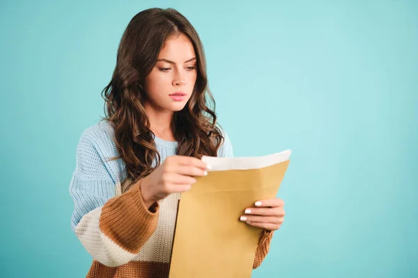 Pensive meisje in gebreide trui bedachtzaam openen reactie envelop over blauwe achtergrond — Stockfoto
