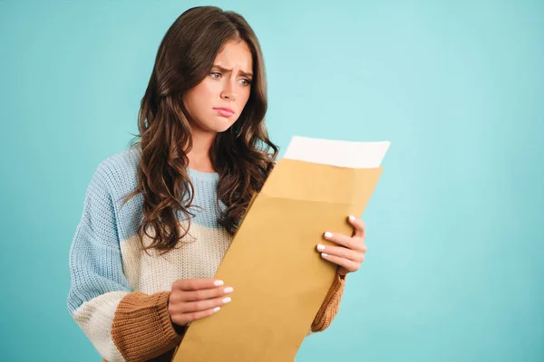 Menina perturbada em camisola de malha, infelizmente abrindo envelope resposta sobre fundo azul — Fotografia de Stock