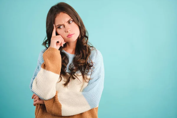 Serious girl in knitted sweater showing deep in thoughts expression over colorful background