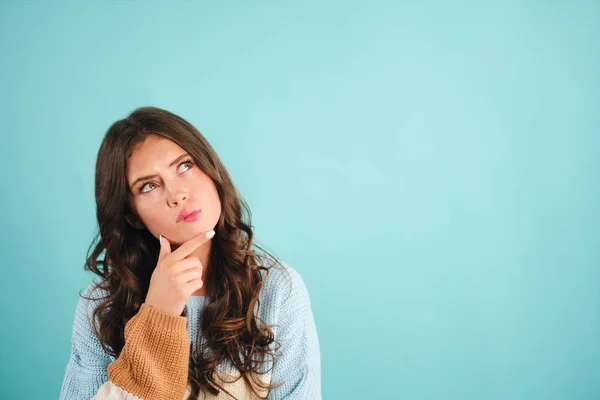 Aantrekkelijk attent meisje in gebreide trui dromend over blauwe achtergrond — Stockfoto