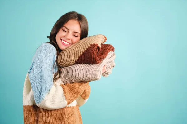 Hermosa linda chica sonriente abrazando soñadoramente acogedores suéteres de punto sobre fondo azul —  Fotos de Stock